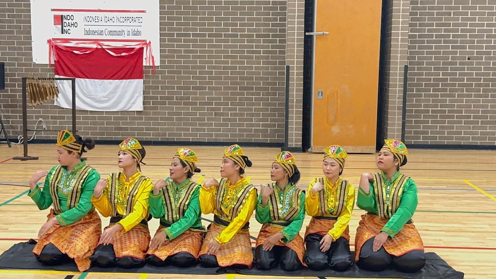 Seven dancers in green and gold costumes kneeling in a row to perform the Saman dance from Aceh